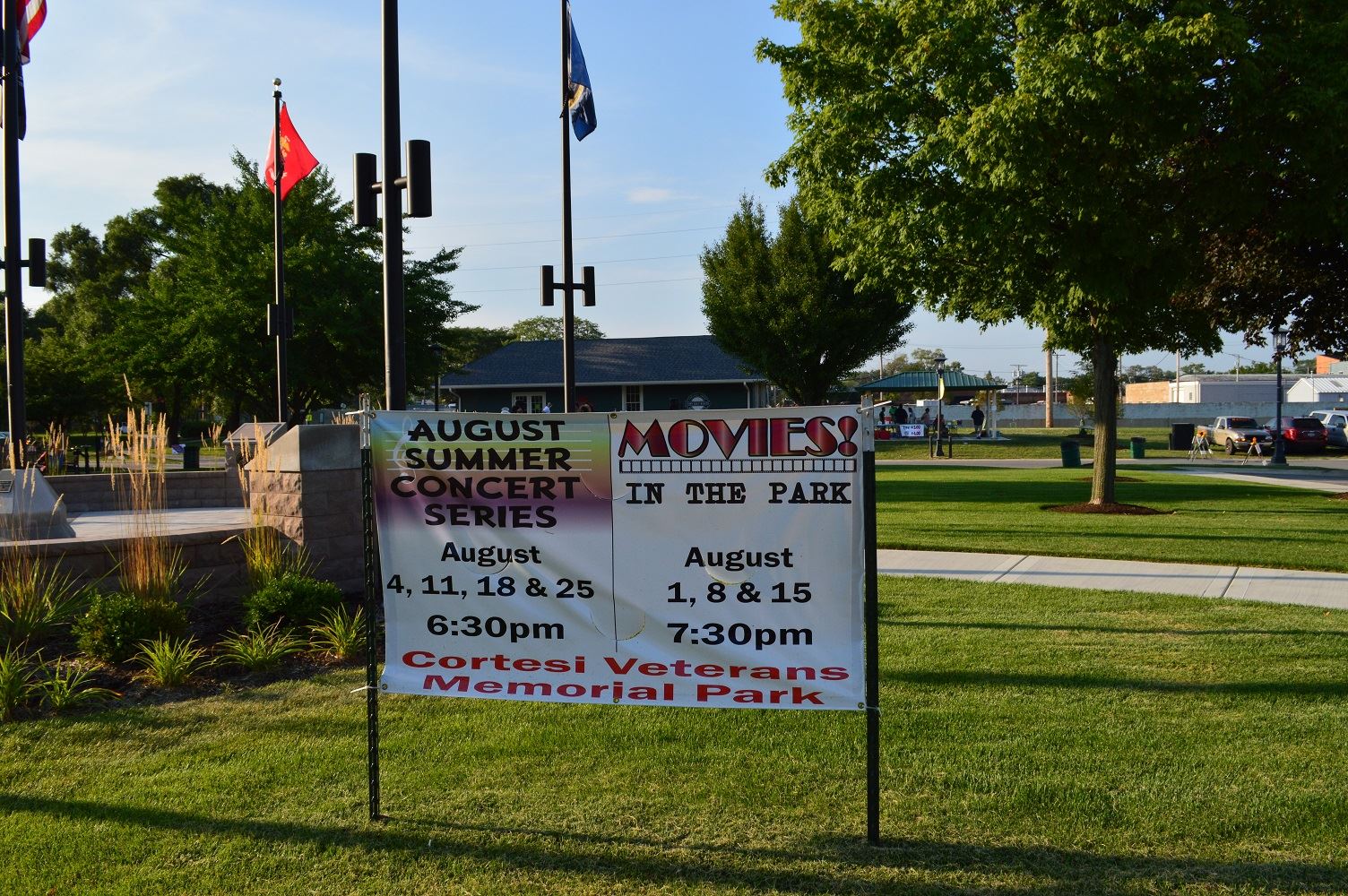 A sign in Cortesi Veterans Memorial Park lists upcoming concerts on Thursdays in August and movies on Mondays in August.